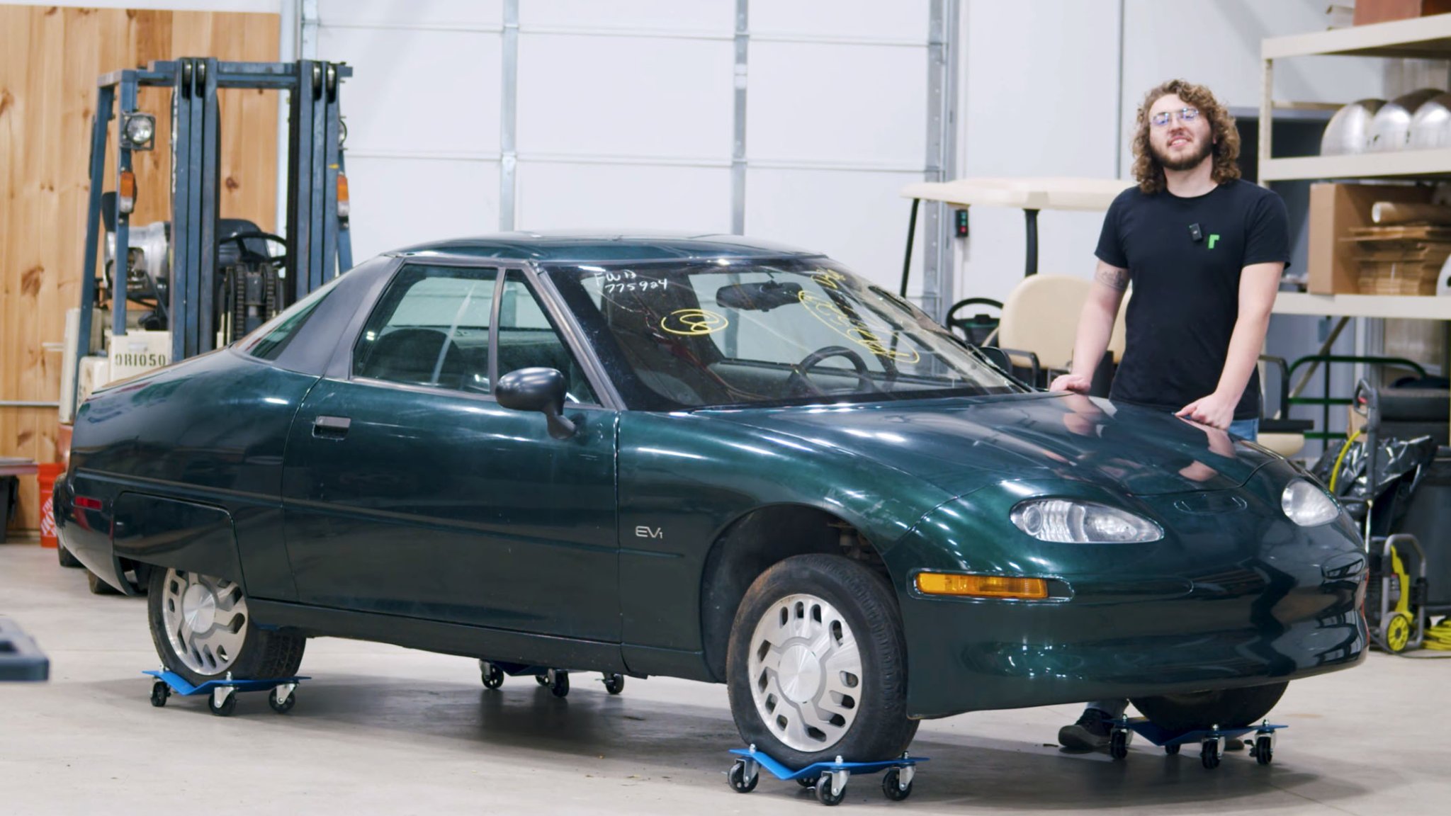 Screenshot of a video showing a person standing next to a GM EV1 in a garage.