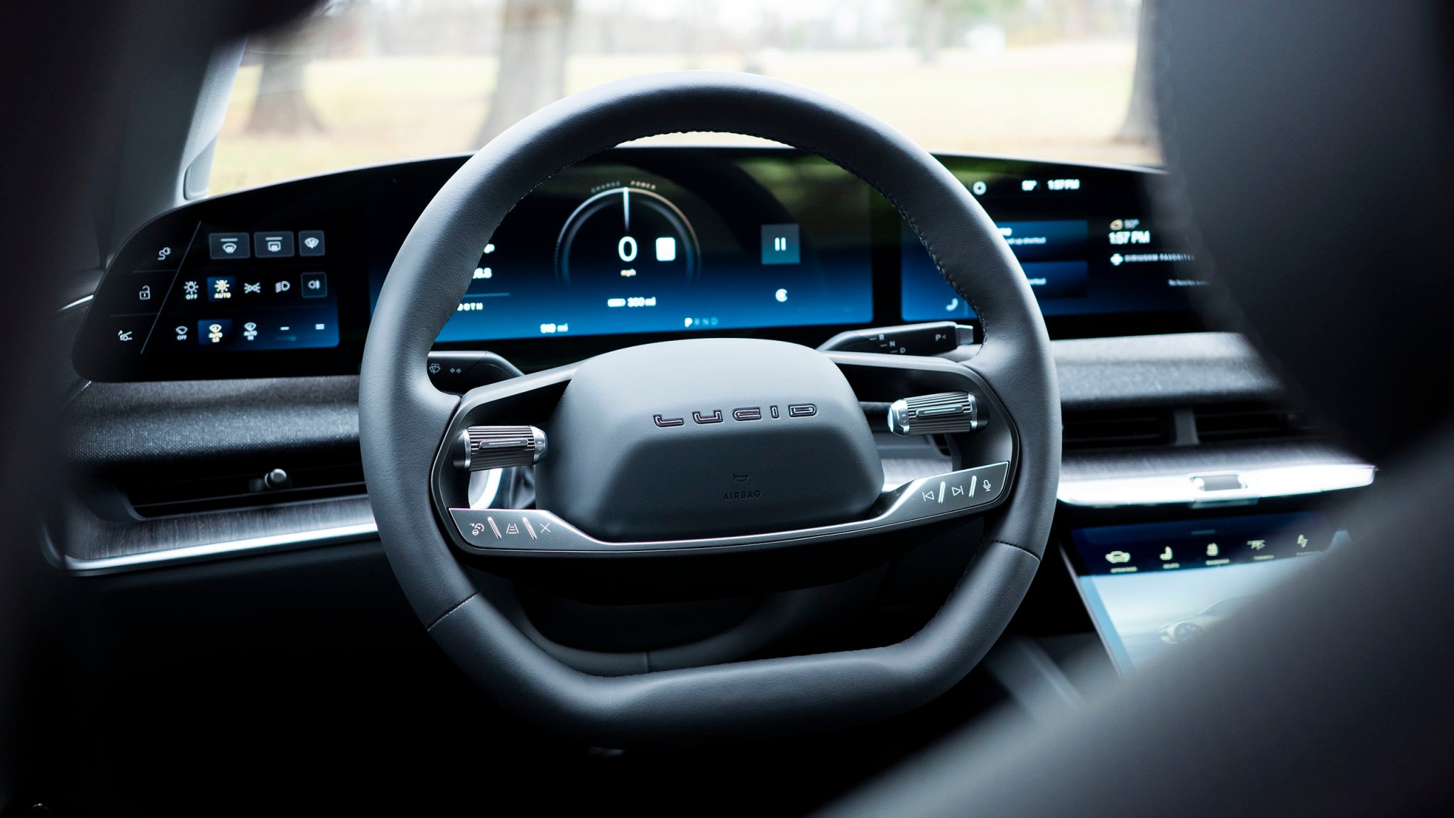Photo of a Lucid Air's steering wheel and instrument cluster taken from behind the driver's headrest and B pillar.