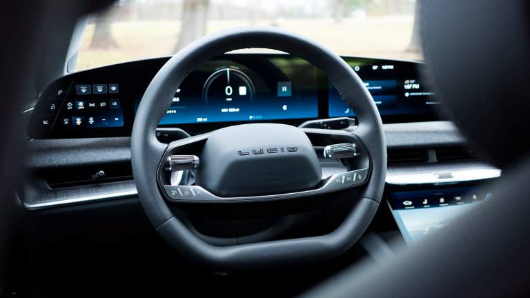 Photo of a Lucid Air's steering wheel and instrument cluster taken from behind the driver's headrest and B pillar.