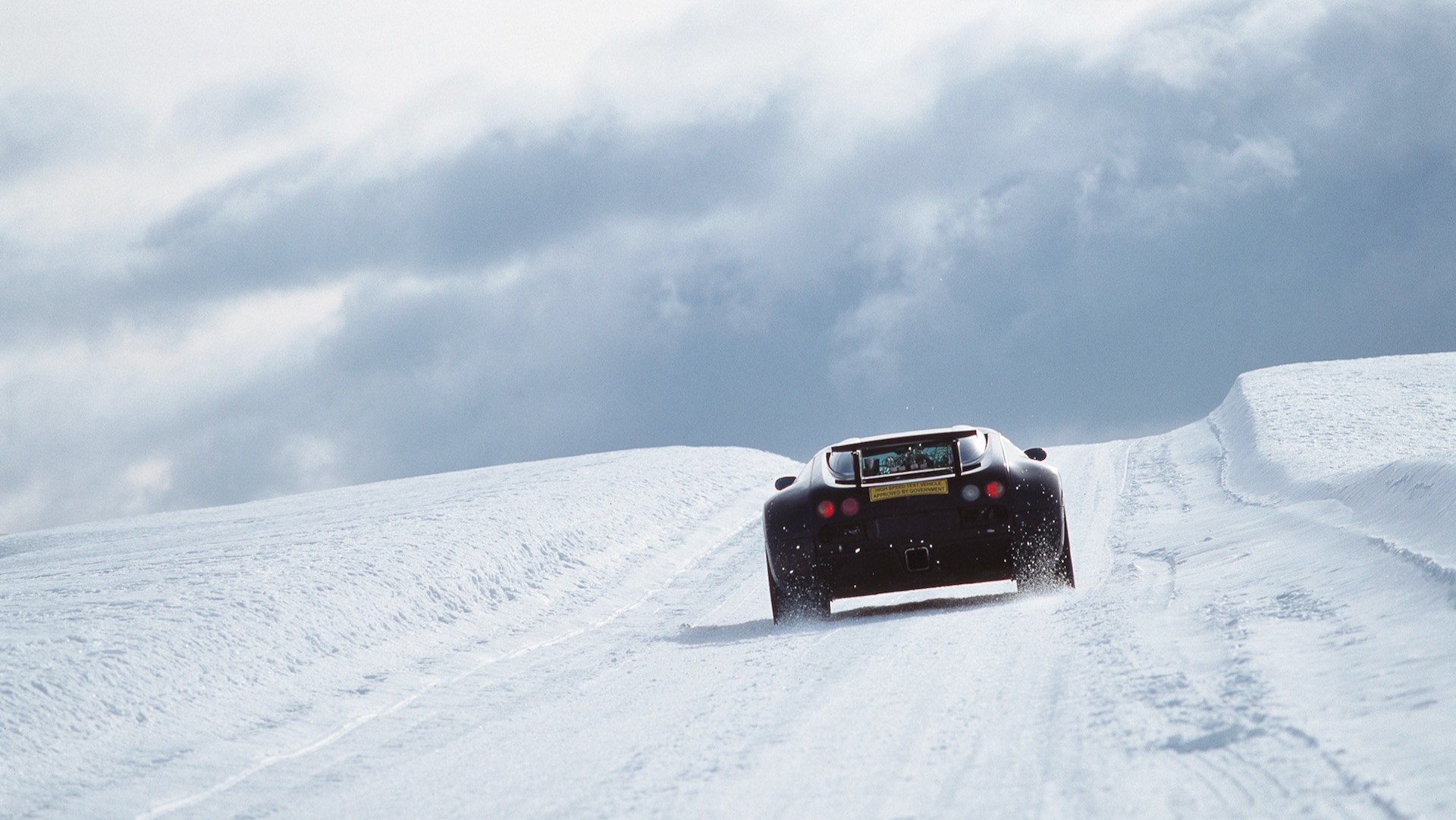 Rear view of a Bugatti Veyron prototype driving up a snow-covered hill.