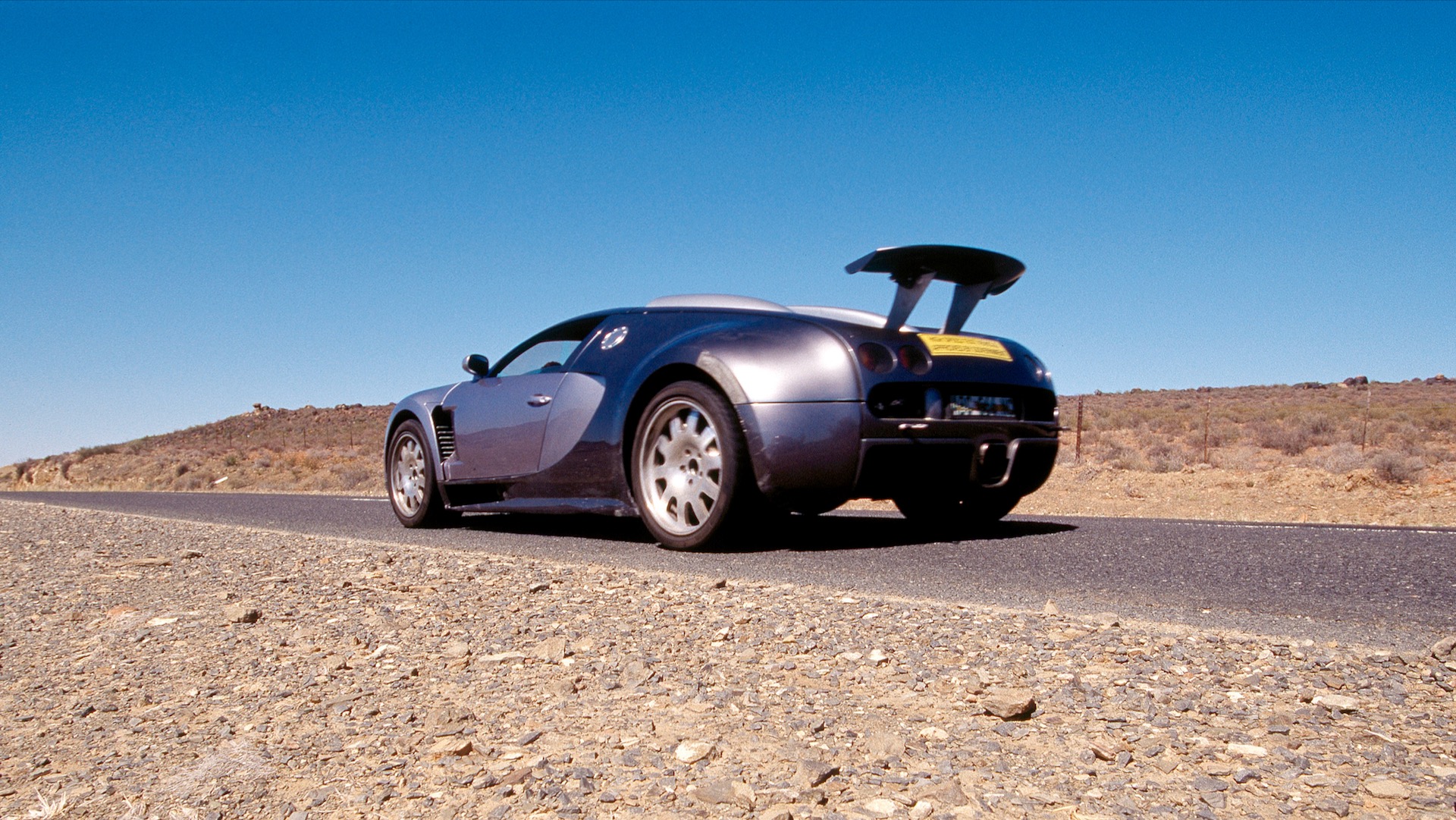 Rear quarter view of a silver Bugatti Veyron prototype with rear spoiler deployed.