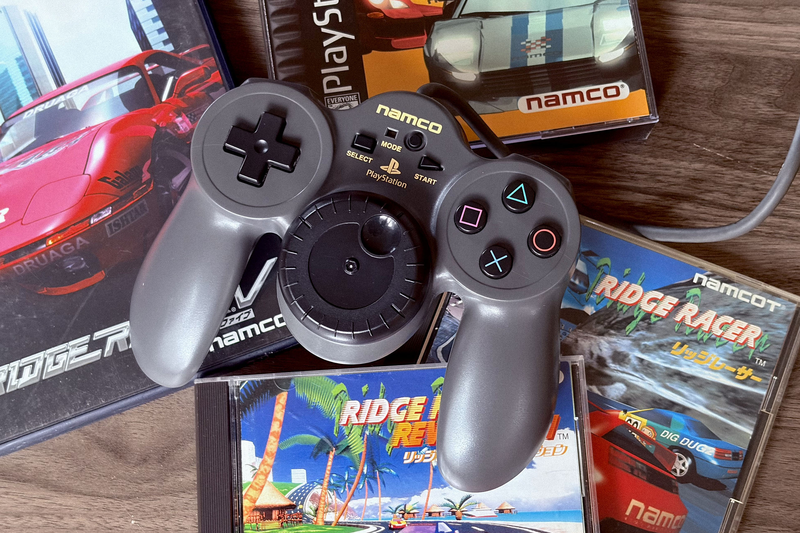 Picture of a Jogcon controller sitting on top of Ridge Racer game cases