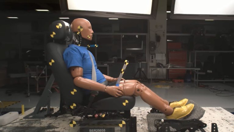 Crash test dummy seated in sled for IIHS whiplash prevention test.