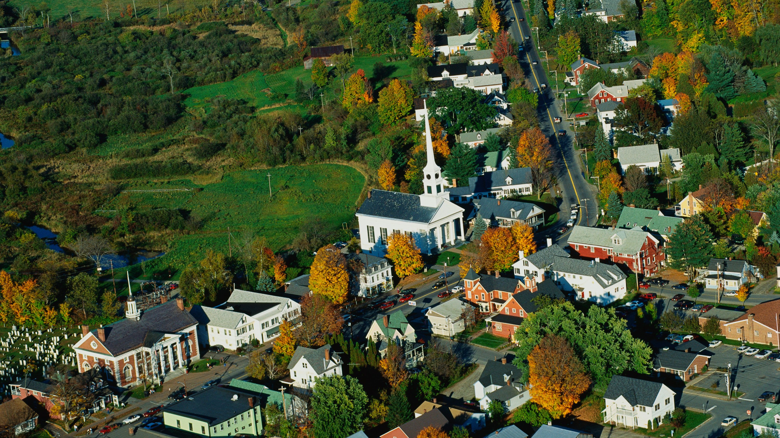 This is an aerial view of the New England village of Stowe, It is along scenic Route 100, There is autumn foliage in the trees, There is a large white church with tall steeple at the center with rows of smaller buildings alongside it on Route 100, It is a typical looking small New England town. (Photo by: Joe Sohm/Visions of America/Universal Images Group via Getty Images)