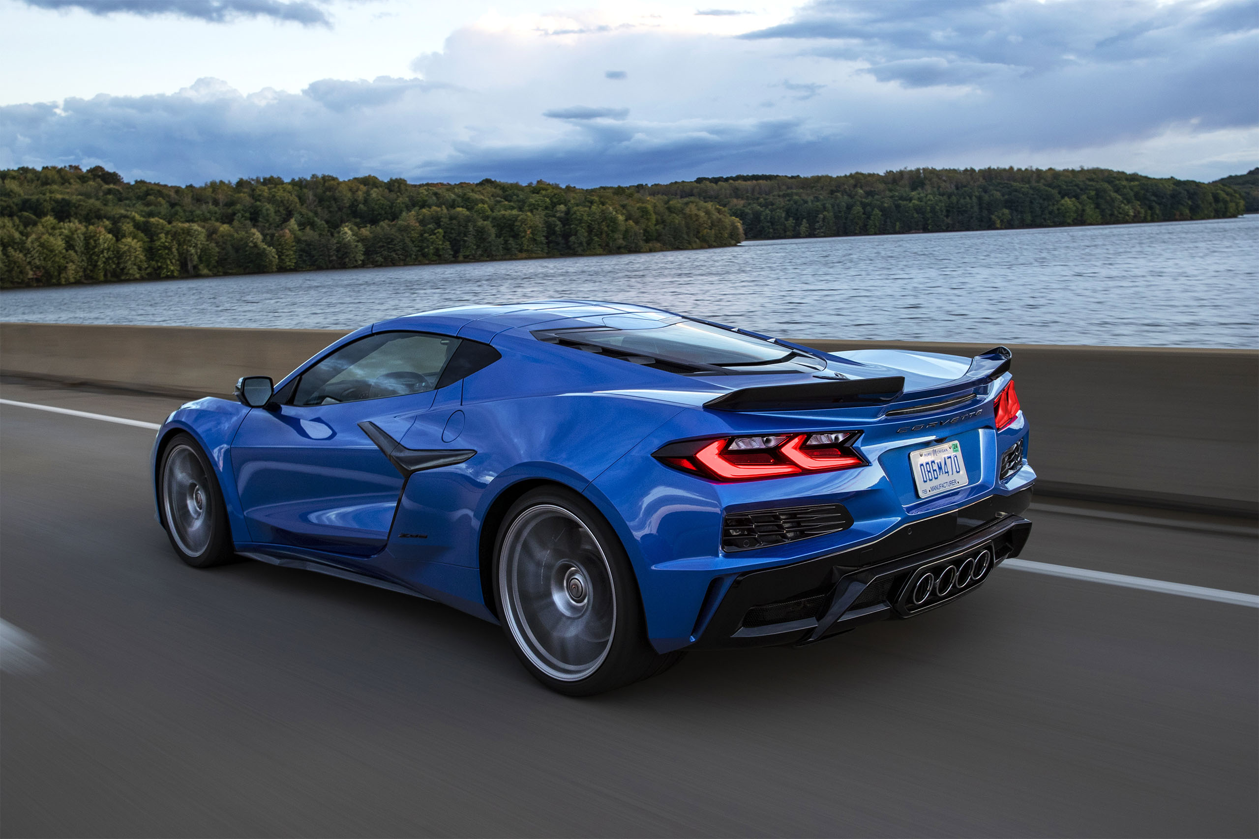Rear 7/8 view of 2023 Chevrolet Corvette Z06 in Elkhart Lake Blue Metallic driving down a road.