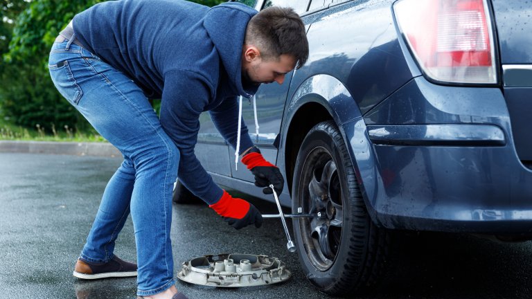 Young man changing flat tire on his car after road accident