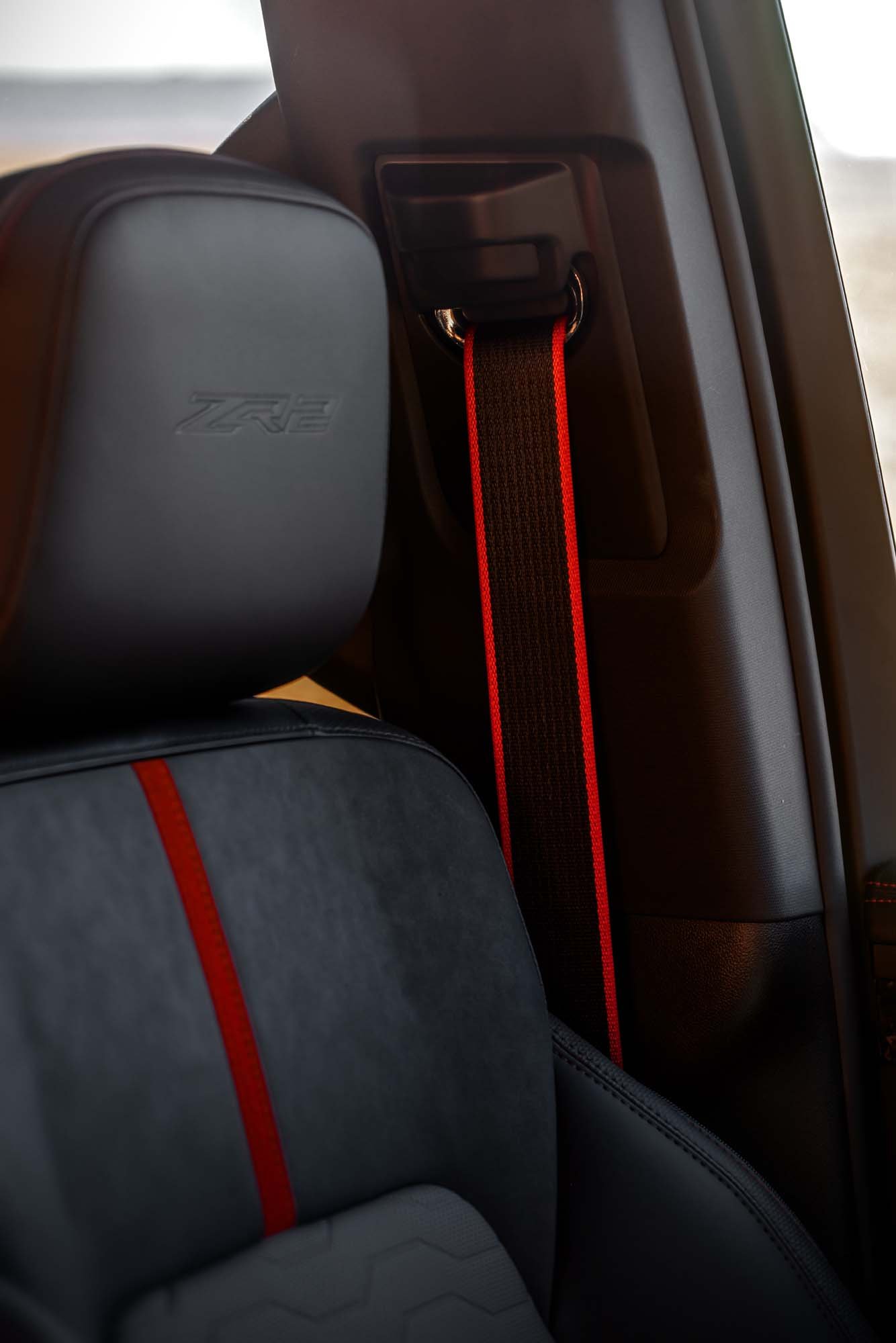 2027 Chevrolet Silverado 1500 ZR2 with Dark Galvinized Interior. Interior detail image focused on the front seat headrest, highlighting Torch Red detailing in the seat, Torch Red edged seatbelt and the debossed ZR2 logo headrest.