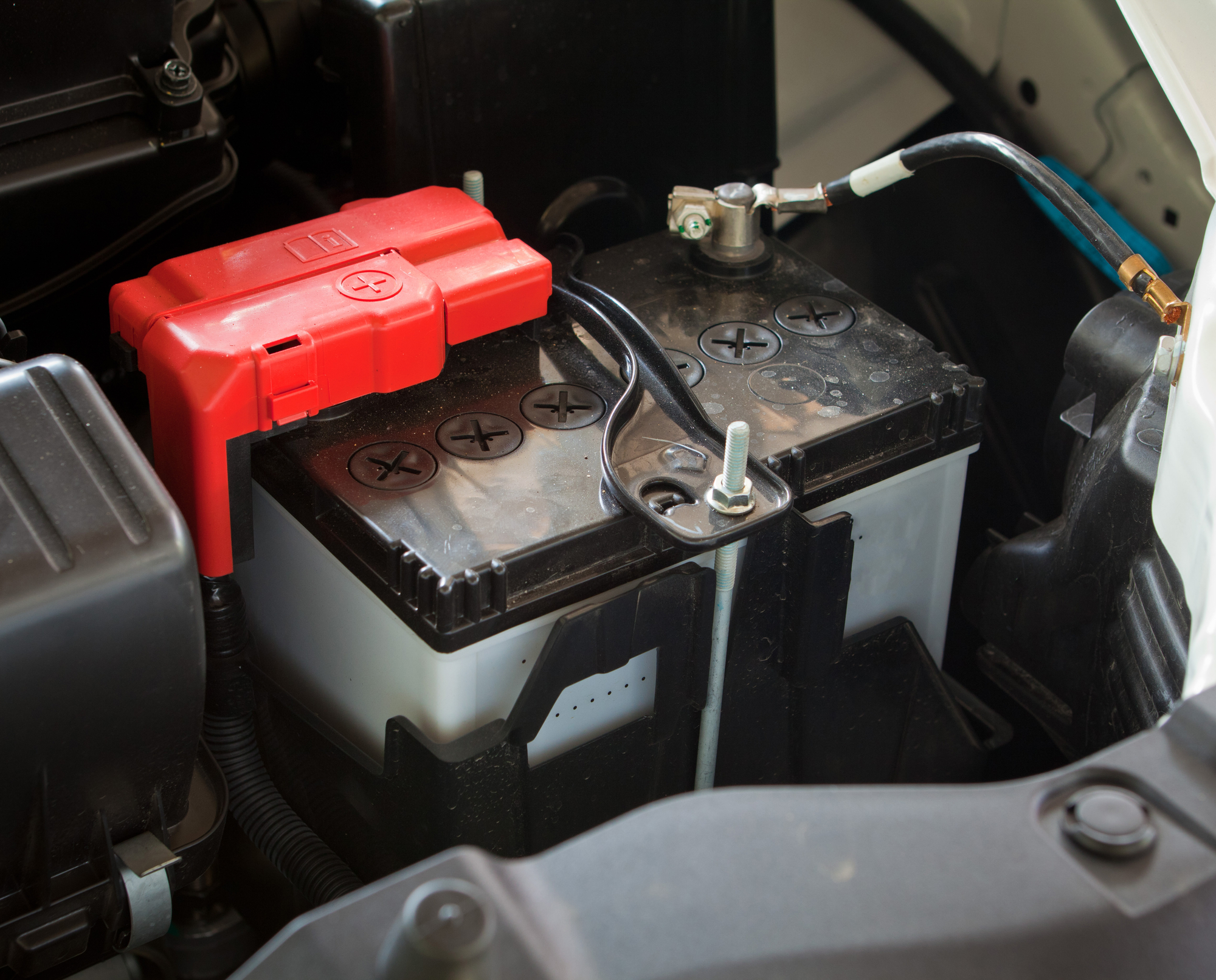 A car battery is shown with a red positive terminal cap.