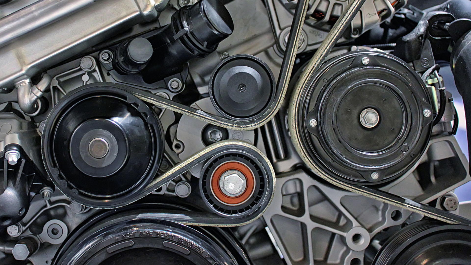 A closeup of an engine and its serpentine belt wrapping around pulleys.