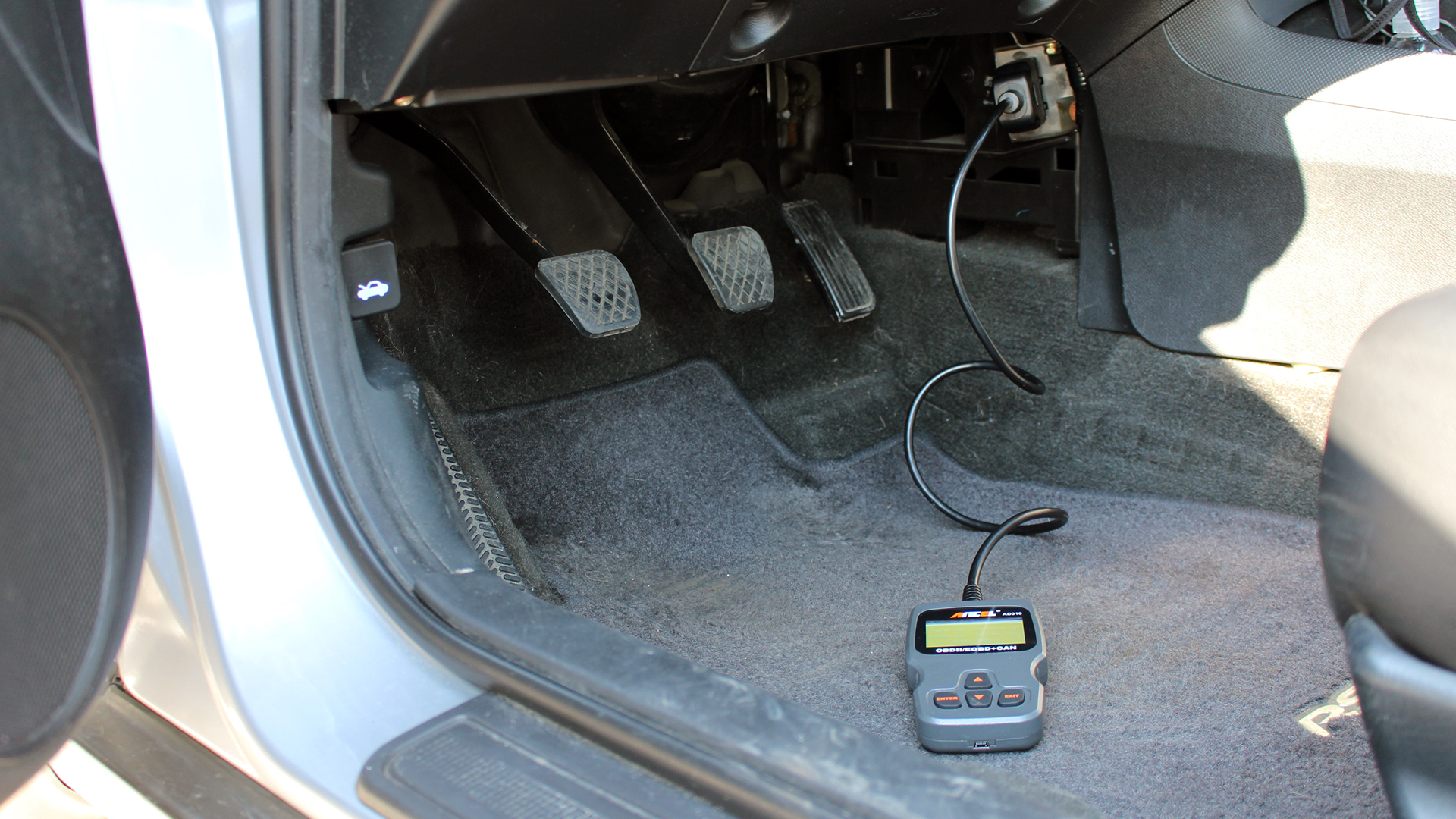 An Ancel OBD scanner in an Acura RSX footwell.
